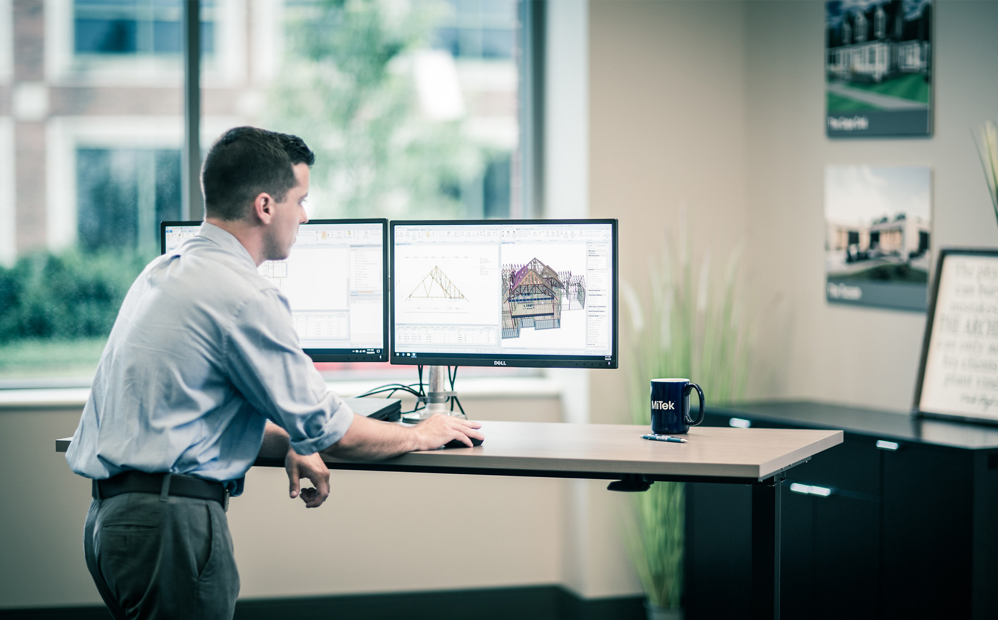 Rozwiązania i usługi oferowane przez MiTek - Mężczyzna stojący przy biurku, pracujący przy komputerze nad modelem 3D domu
