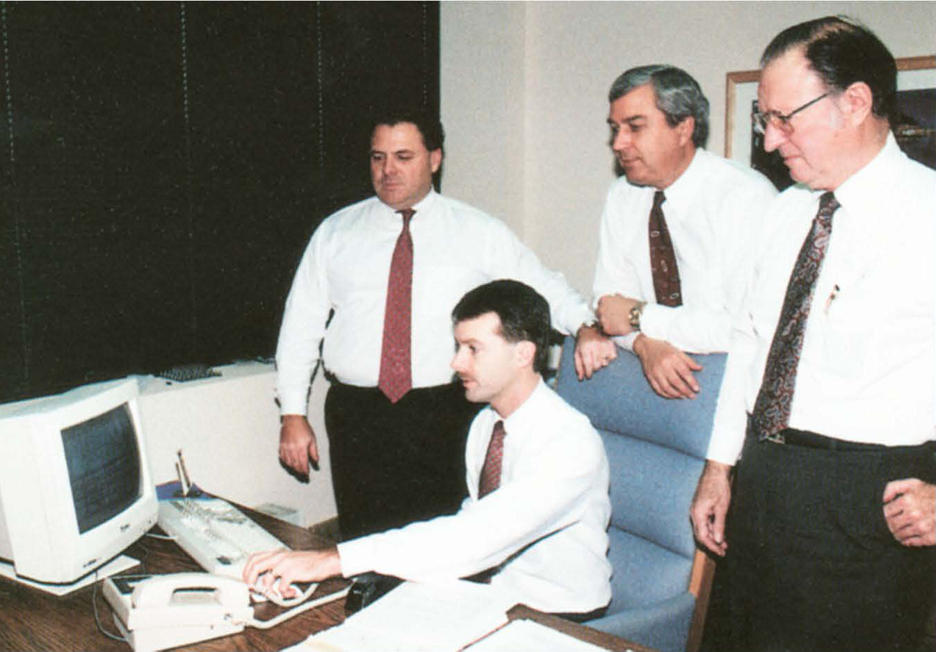 Die Geschichte von MiTek - Dave McQuinn und drei Männer an einem Schreibtisch mit einem Computer aus den späten 1980er Jahren