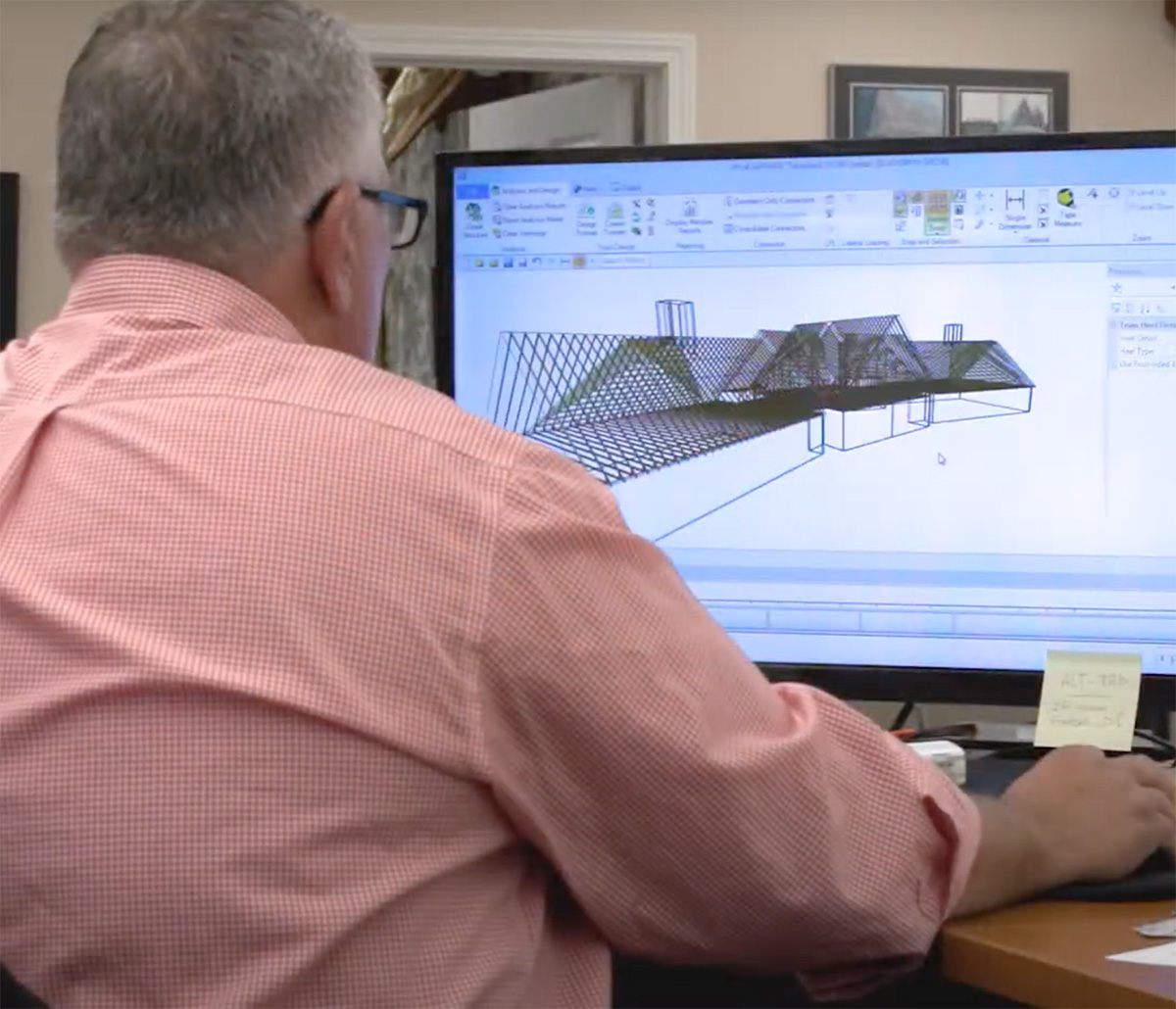 MiTek Design Support Services - Mann sitzt am Schreibtisch und arbeitet am Computer mit einem 3D-Modell auf dem Bildschirm